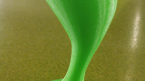 In der Mitte steht eine dunkelgrüne, tropfenförmige Skulptur, in etwa handgroß und länglich, die einer Skulptur in der Informatikfakultät nachempfunden ist. Der boden ist ebenfalls hellgrün und im Hintergrund ist der Sockel der echten Skulptur aus dem APB