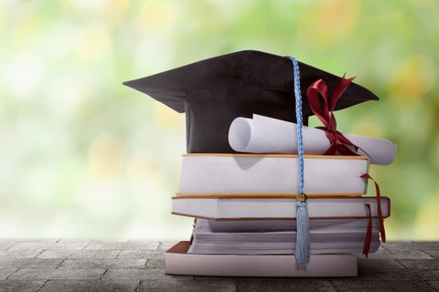 The photo shows a small stack of books. A doctor's hat is standing on it. A diploma lies next to it.