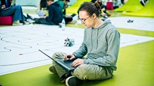 Student mit Laptop vor Planeten des RoboLabs im Foyer des APB sitzend