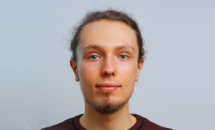 Profilfoto von Tobias Hänel. Er hat blaue Augen, dunkle zu einem Dutt zusammengebunden Haare und einen kurzen Bart. Er trägt einen dunkelroten Pullover.