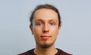 Profilfoto von Tobias Hänel. Er hat blaue Augen, dunkle zu einem Dutt zusammengebunden Haare und einen kurzen Bart. Er trägt einen dunkelroten Pullover.