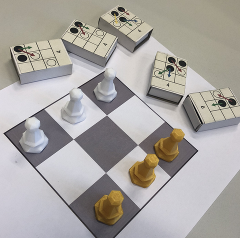 Auf dem Bild ist ein 3x3 Schachfeld mit Figuren zu sehen. Daneben liegen Streichholzschachteln, auf denen mögliche Stellungen und Züge abgebildet sind.