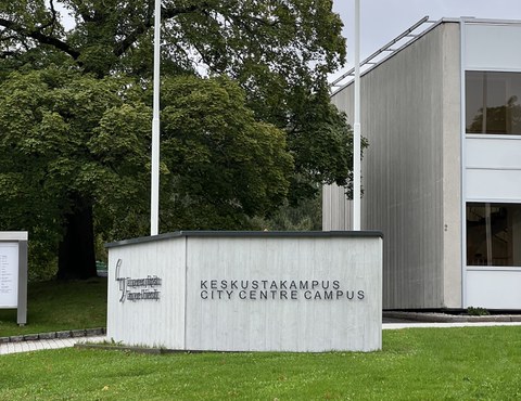 Im Vordergrund grüne Wiese, im Hintergrund das Zeichen der University of Tampere