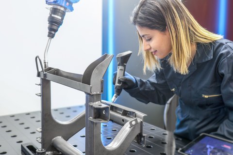 Maschinenbedienerin lernt einen Industrieroboter mit einem handgeführten Tool an.f
