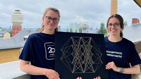 Vorstellung Lange Nacht der Wissenschaften, zwei Personen mit Deko zu Neuronalen Netzen, im Hintergrund der Campus der TU Dresden