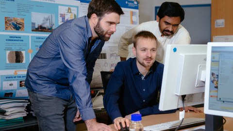 Photo of three employees working on a computer