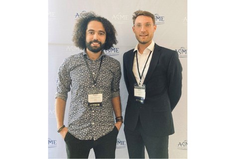 Herr Guesmi und Herr Manthey, nebeneinander stehend und lächelnd, bei der Konferenz.