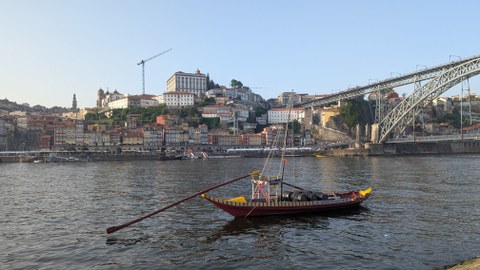 Stadtansicht von Porto, im Vordergrund der Fluss und ein Fischerboot, im Hintergrund die in den Felsen gebaute Stadt.