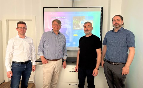 4 Männer schauen nach dem Meeting für ein Gruppenfoto in die Kamera, hinter Ihnen die Website von Pro3 mit der geöffneten Unterseite der TU Dresden.