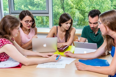 Foto von fünf Studenten, die in einer Workshoprunde zusammen am Laptop lernen.