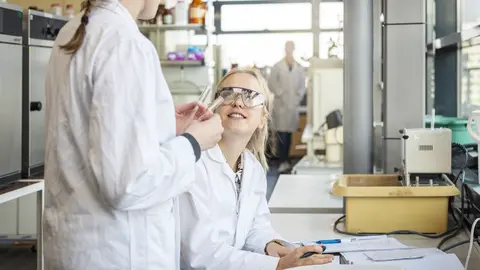 Zwei Frauen unterhalten sich im Labor. Eine davon hält zwei Reagenzgläser in der Hand.