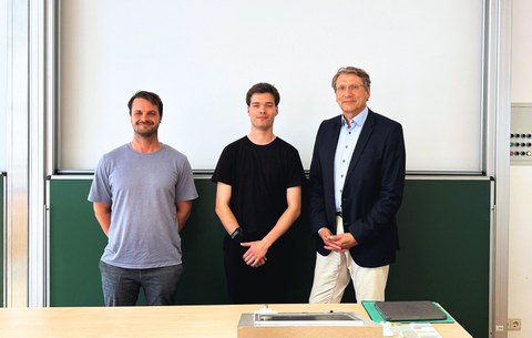 Luis Wunder, Richard Stephan und Prof. M. Beckmann, nebeneinander stehend vor einer Tafel nach der Verteidigung der Arbeit.