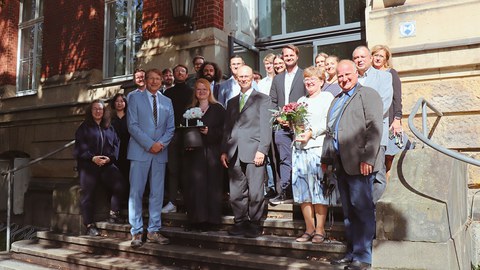 Die Gruppe der Gäste und Kollegen der Promovierenden stehen auf der Treppe eines Gebäudes für ein Gruppenfoto zusammen.