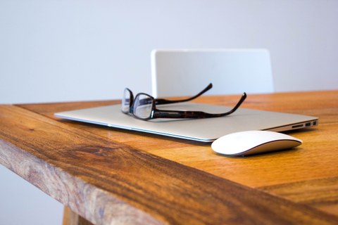 Foto von einem Arbeitsplatz, mit einem Laptop, einer Maus und einer Brille