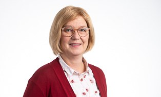 Frau mit kinnlangen blonden Haaren, Brille und heller Bluse mit roter Jacke