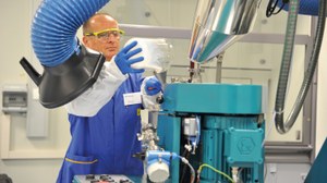 Das Foto zeigt einen Mitarbeiter, der in einer Technikumshalle ein weißes Pulver in ein mannshohes Aggregat zur Herstellung keramischer Schlicker einfüllt.