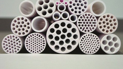 Front view of a pile of ceramic filtration tubes, varying in the number, size and shape of the internal channels.