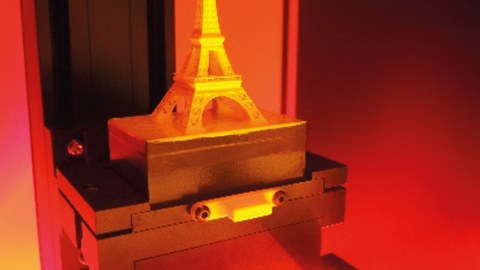 A freshly formed miniaturized modell of the Eiffel tower is standing on the working top of a 3D printer (photograph).