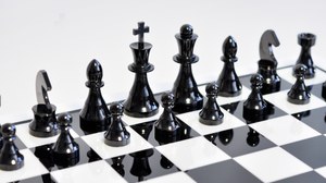 Das Foto fokussiert auf die schwarzen Figuren eines keramischen Schachspiels.