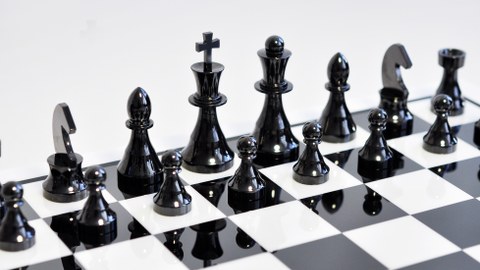 Das Foto fokussiert auf die schwarzen Figuren eines keramischen Schachspiels.