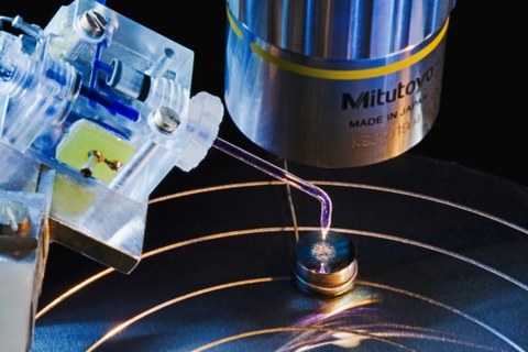 Eine elektrochemische Mikrokapillarzelle - bestehend aus einem Kunstftoffkörper und einer dünn ausgezogenen Glaskapillare - wird unter dem Objektiv eines Mikroskops auf eine Metallprobe aufgesetzt.