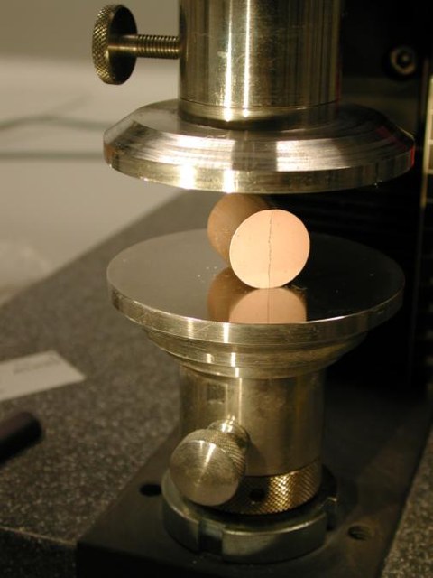 Ein zylindrischer Grünkörper ist zischen zwei Metallstempeln eingespannt, um die Druckfestigkeit zu messen.