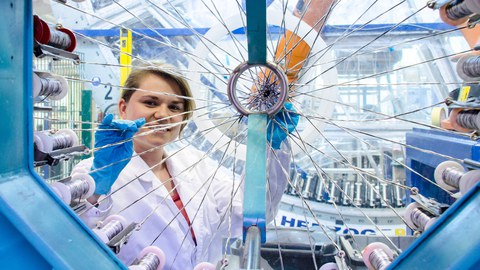 Eine Mitarbeiterin des Instituts für Leichtbau und Kunststofftechnik steht am kleinen Flechtrad.