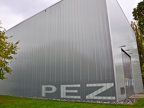 Außenaufnahme einer großen, grauen, glasähnlichen Werkhalle auf der die Buchstaben PEZ zu lesen sind.