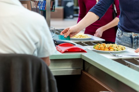 Das Foto zeigt einen Kassenbereich in der Mensa der TU Dresden. Eine Person bezahlt in diesem Moment mit ihrer Mensakarte ihr Essen.