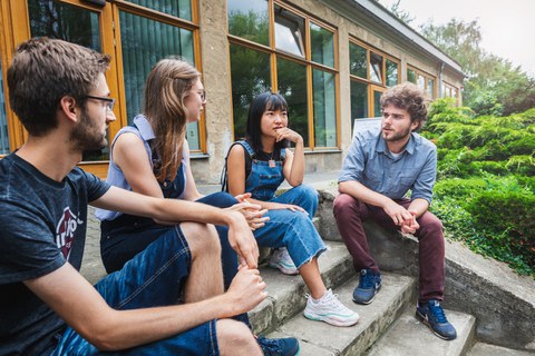 Im Freien sitzen vier ERASMUS Studenten auf einer Treppe und unterhalten sich.