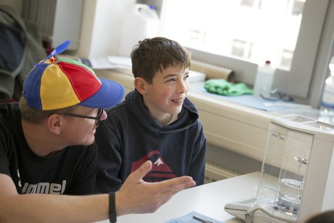 A technician explains something to a boy. The boy looks up into the air and seems to be thinking. In front of him is a density meter.