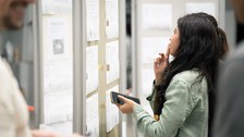 Eine Studentin steht an einer Pinnwand und sieht sich interessiert die Arbeitsangebote an.