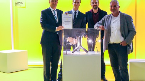 Eine Gruppe von vier Wissenschaftlern steht vor einer Messevitrine aus der Fachmesse Materialica in München.