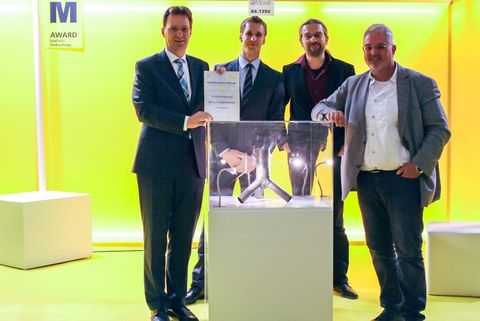 Eine Gruppe von vier Wissenschaftlern steht vor einer Messevitrine aus der Fachmesse Materialica in München.