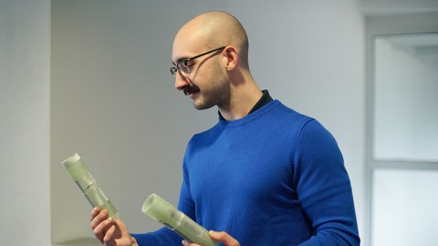 Ein Mann mit Brille und Glatze blickt auf Bauteile, die er in der Hand hält.