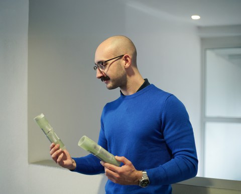 Ein Mann mit Brille und Glatze blickt auf Bauteile, die er in der Hand hält.