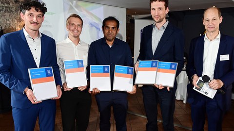 Gruppenfoto von fünf Personen. Sie halten Urkunden in der Hand und lächeln in die Kamera.