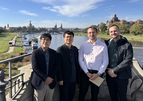 Gruppenfoto: vier Personen schauen lächelnd in die Kamera. Im Hintergrund: die Elbe, Carolabrücke und die Skyline der Altstadt mit Frauenkirche, Hofkirche, Schloss.