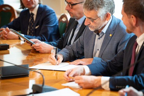 A man with short grey hair signs a document.