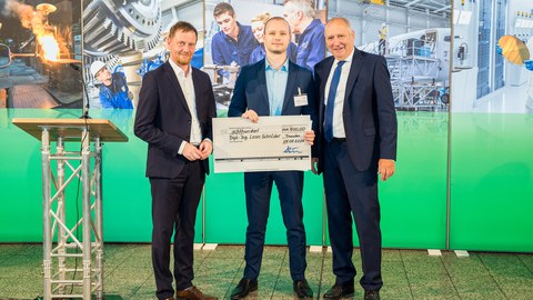 Three people look into the camera. The person in the middle is holding a cheque for €800.