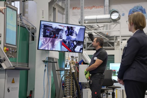 Eine Person schaut in einen Fernseher, der an eine Maschine angeschlossen ist. Der Fernseher zeigt vier verschiedene Kamerabilder, die unterschiedliche Prozesse in der Maschine zeigen.