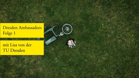 Aufnahme einer Frau aus der Vogelperspektive. Sie schaut nach oben in die Kamera und steht auf Rasen. Neben ihr liegt ein E-Bike. Eingeblendet ist die Schrift "Dresden Ambassadors, Folge 1 mit Lisa von der TU Dresden".