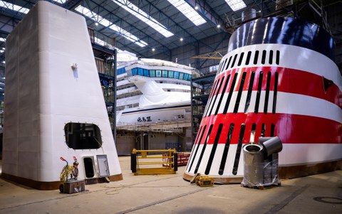 Die Hallen einer Werft. Mittig: ein großes Schiff, links und rechts weitere große Teile für den Schiffbau.