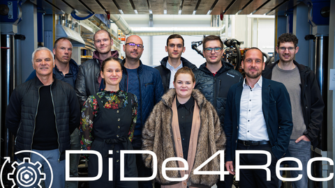 Zehn Personen (acht Männer, zwei Frauen) stehen vor einer hydraulischen Presse und schauen lächelnd in die Kamera. Auf de, Foto befindet sich das DiDe4Rec-Logo.