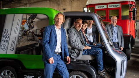 Menschen schauen lächelnd in die Kamera. Ein Teil dieser Menschen sitzt in dem Auto.