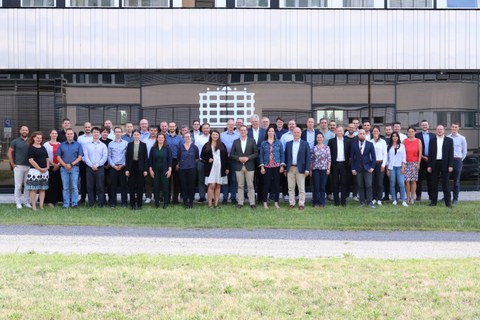 Gruppenfoto von etwa 50 Personen, die in die Kamera schauen und lächeln. Sie stehen draußen vor einem Gebäude, das im Hintergrund zu sehen ist.