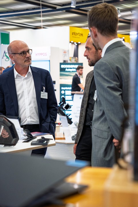 Drei Herren stehen in einer kleinen Gruppe und reden ernsthaft miteinander.