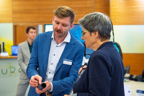 Ein junger Mann zeigt eber Frau ein Bauteil. Sie schaut interessiert auf den Demonstrator.