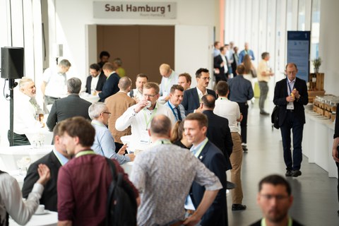 Menschen stehen in einem Foyer, reden, lachen, trinken Kaffee.