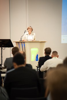 Eine Frau steht an einem Rednerpult und hält eine Rede.